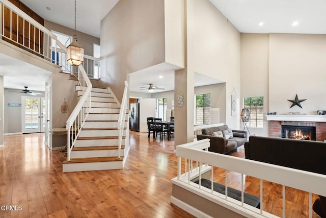 living room featuring a towering ceiling, a healthy amount of sunlight, light hardwood / wood-style floors, and a brick fireplace