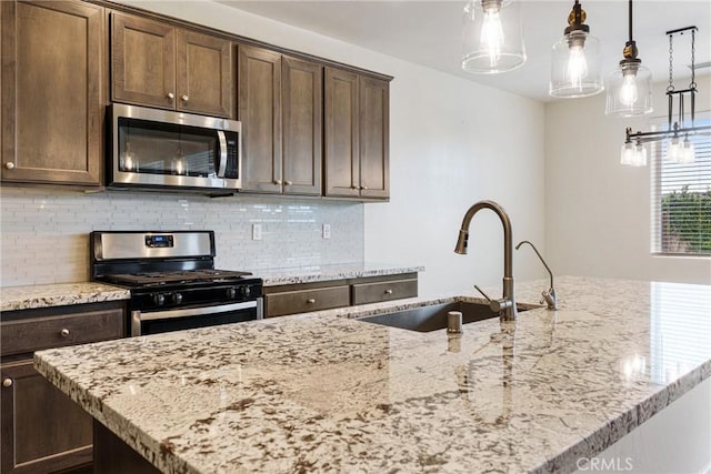 kitchen with tasteful backsplash, light stone counters, a kitchen island with sink, stainless steel appliances, and a sink