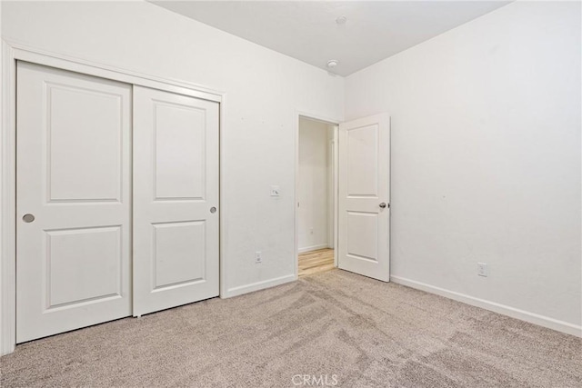 unfurnished bedroom with baseboards, a closet, and light colored carpet