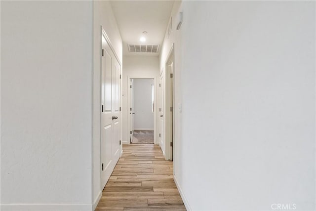 hallway featuring light wood-type flooring, visible vents, and baseboards