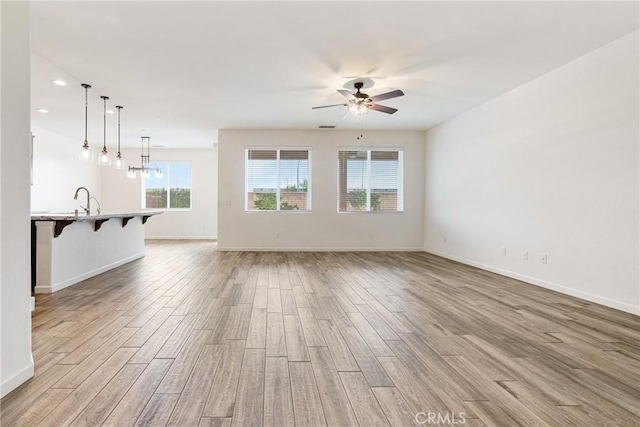 unfurnished living room featuring a ceiling fan, light wood-style flooring, and baseboards