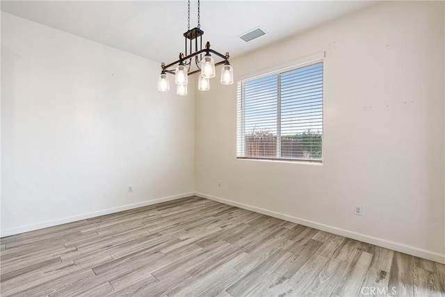 empty room featuring a chandelier, visible vents, light wood-style flooring, and baseboards