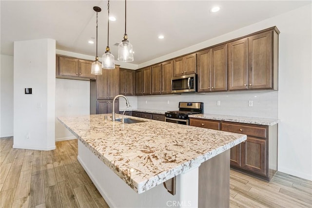 kitchen with stainless steel appliances, light wood-type flooring, a sink, and light stone countertops