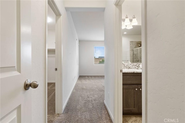 hallway featuring a sink, baseboards, carpet flooring, and a textured wall