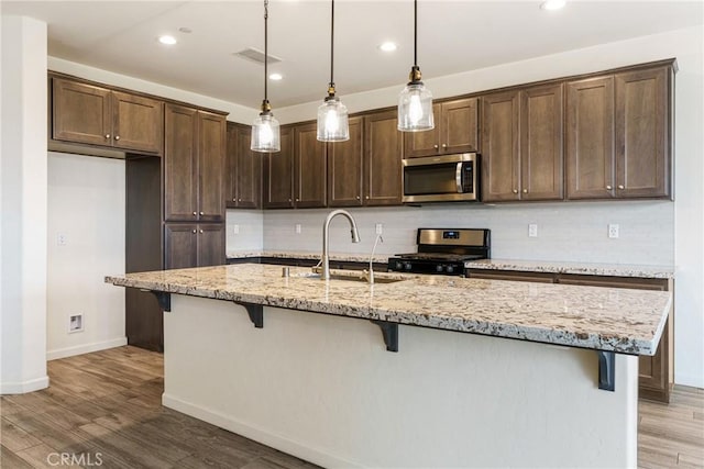 kitchen with decorative backsplash, range with gas stovetop, stainless steel microwave, light wood-style floors, and a sink