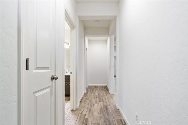 hallway featuring a textured wall, light wood-style flooring, and baseboards