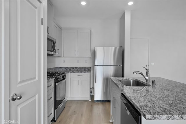 kitchen featuring sink, light wood-type flooring, appliances with stainless steel finishes, light stone countertops, and white cabinets