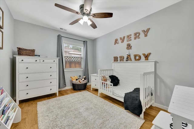 bedroom with ceiling fan, a crib, and light wood-type flooring