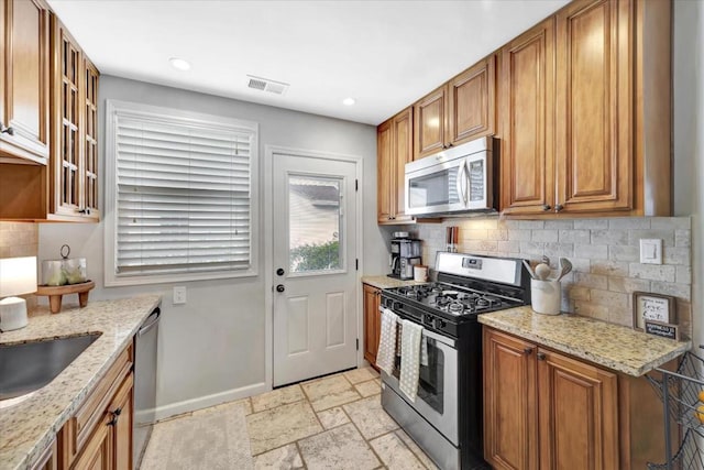 kitchen featuring tasteful backsplash, light stone countertops, and appliances with stainless steel finishes