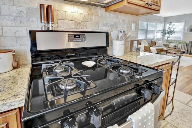 interior details with light stone counters, gas range oven, light hardwood / wood-style floors, and decorative backsplash