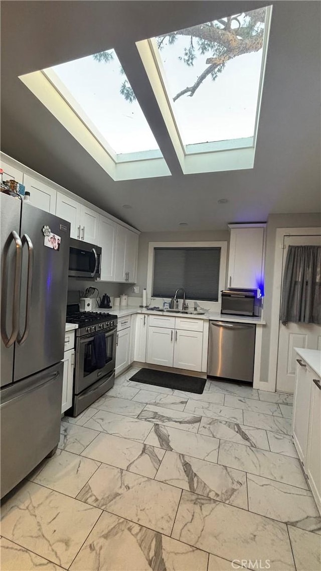 kitchen with white cabinetry, appliances with stainless steel finishes, sink, and lofted ceiling with skylight