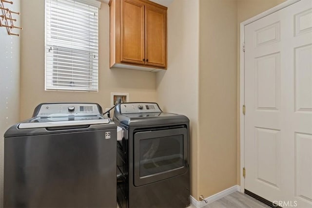 laundry area with washer and clothes dryer, light hardwood / wood-style floors, and cabinets