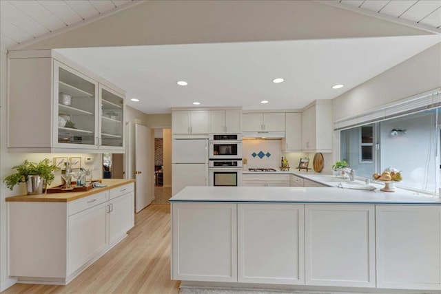 kitchen with lofted ceiling, sink, kitchen peninsula, white appliances, and white cabinets