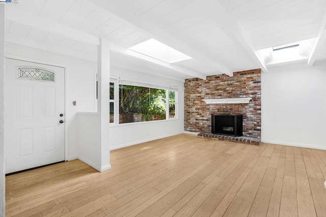 unfurnished living room with beamed ceiling, a brick fireplace, light hardwood / wood-style floors, and a skylight