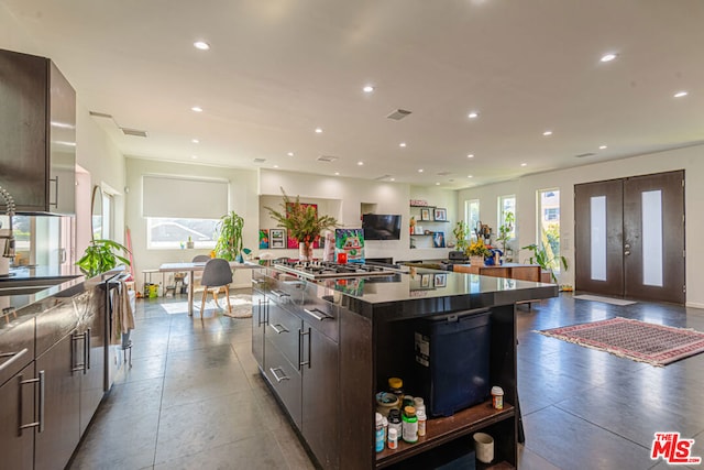 kitchen with french doors, dark brown cabinetry, sink, stainless steel gas cooktop, and a large island