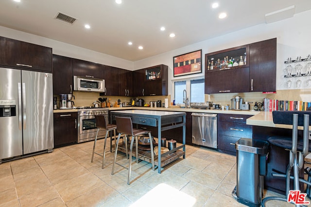 kitchen featuring tasteful backsplash, dark brown cabinets, a kitchen breakfast bar, and appliances with stainless steel finishes