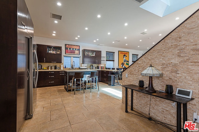 kitchen with dark brown cabinetry, a breakfast bar, stainless steel refrigerator, and a center island