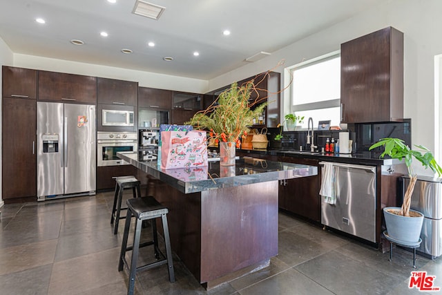 kitchen featuring dark brown cabinets, stainless steel appliances, a breakfast bar, and a kitchen island