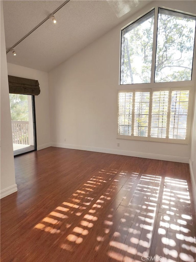 interior space featuring dark hardwood / wood-style flooring, vaulted ceiling, rail lighting, and a textured ceiling