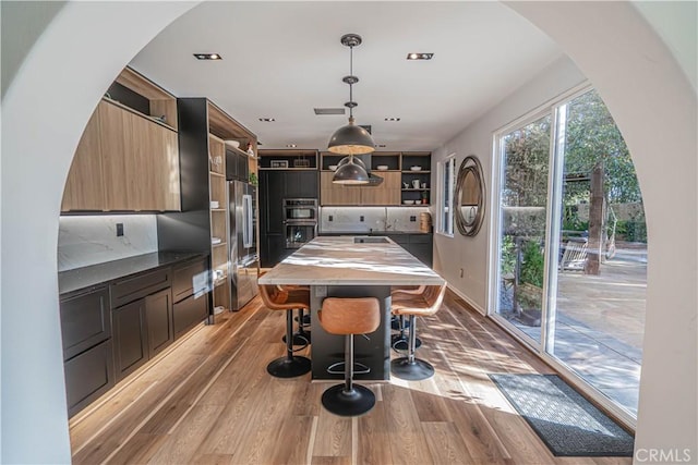 kitchen with hanging light fixtures, double oven, a kitchen breakfast bar, and light hardwood / wood-style flooring