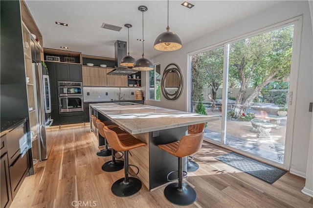 kitchen with appliances with stainless steel finishes, decorative light fixtures, dark stone countertops, island exhaust hood, and a center island