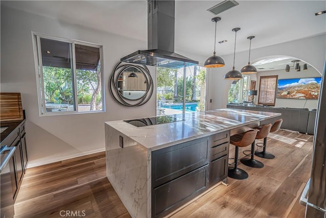 kitchen with light stone counters, hanging light fixtures, island range hood, and hardwood / wood-style flooring