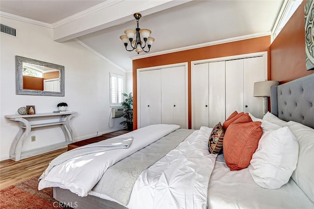 bedroom with a notable chandelier, ornamental molding, lofted ceiling with beams, and two closets