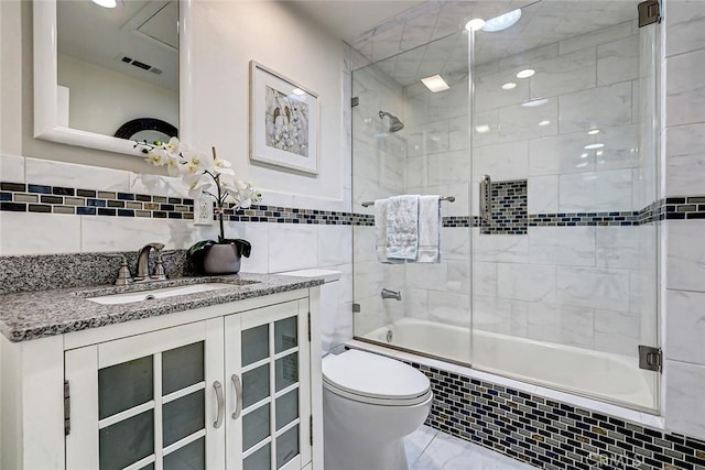 full bathroom with vanity, combined bath / shower with glass door, tile walls, and toilet