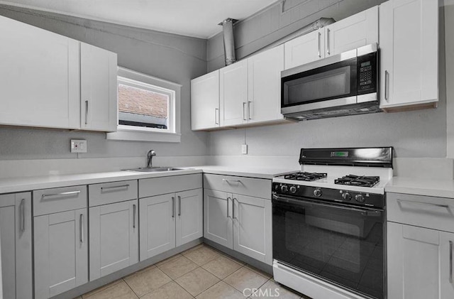 kitchen featuring sink, light tile patterned floors, range with gas stovetop, and white cabinets