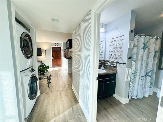 clothes washing area featuring stacked washer / drying machine and light hardwood / wood-style flooring