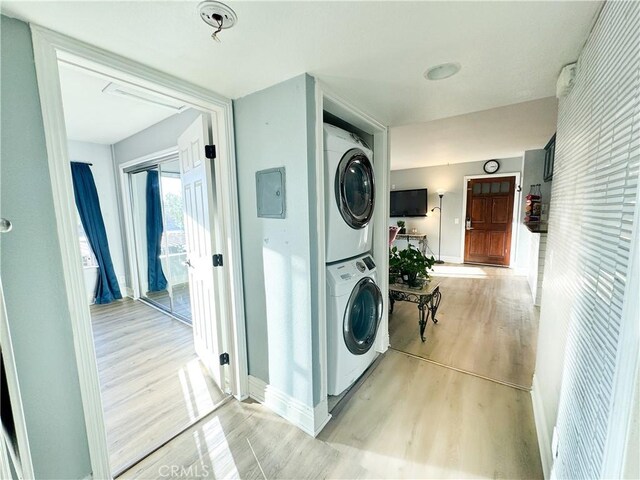 washroom featuring stacked washer / dryer, electric panel, and light wood-type flooring