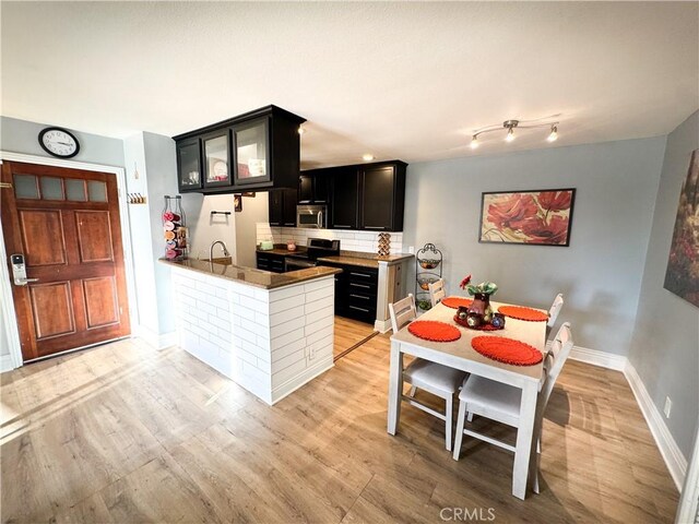 kitchen with sink, backsplash, stainless steel appliances, kitchen peninsula, and light wood-type flooring