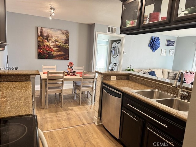 kitchen featuring appliances with stainless steel finishes, sink, stacked washer and dryer, dark brown cabinets, and light wood-type flooring