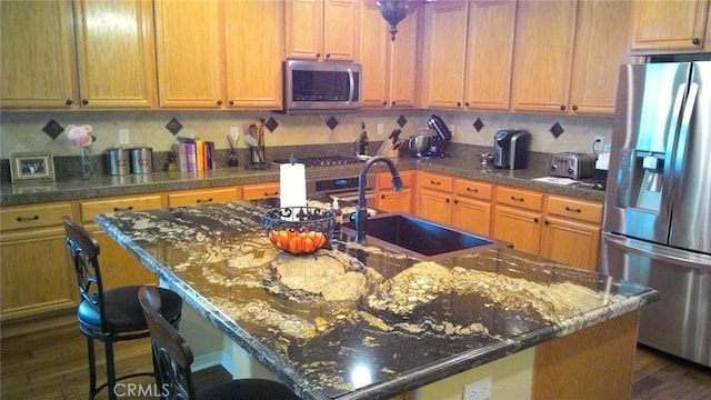 kitchen with an island with sink, stainless steel appliances, a kitchen breakfast bar, and sink