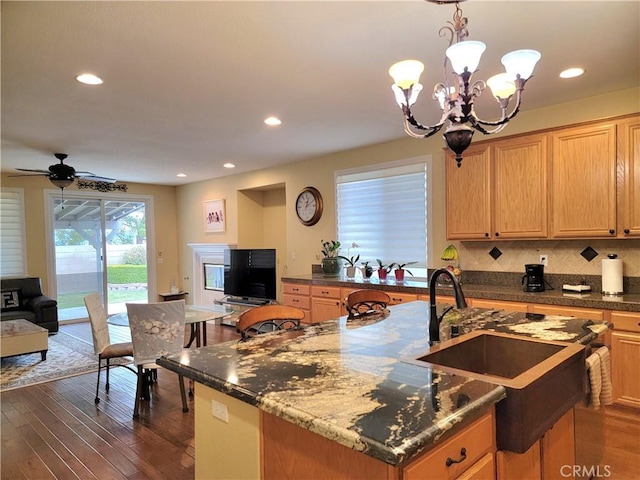 kitchen with a kitchen island with sink, hanging light fixtures, backsplash, dark hardwood / wood-style floors, and ceiling fan with notable chandelier