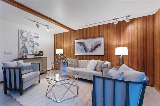 carpeted living room with beam ceiling, wooden walls, and track lighting