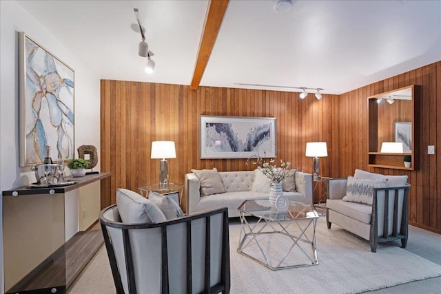 living room featuring beamed ceiling, light colored carpet, rail lighting, and wood walls