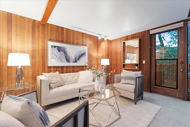 living room featuring beamed ceiling, light colored carpet, track lighting, and wood walls