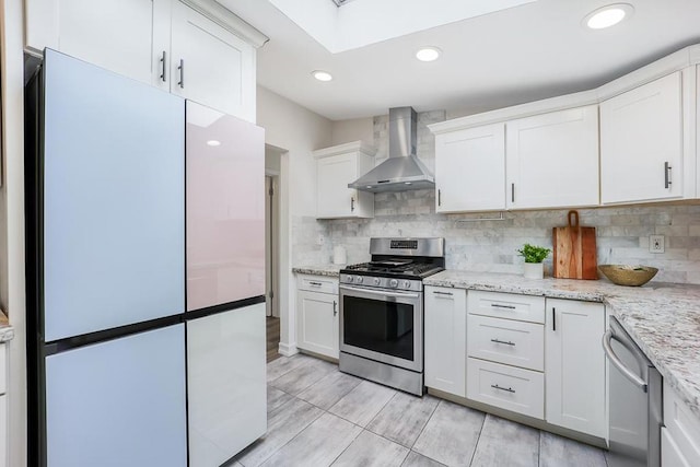 kitchen with white cabinetry, light stone counters, appliances with stainless steel finishes, wall chimney range hood, and backsplash