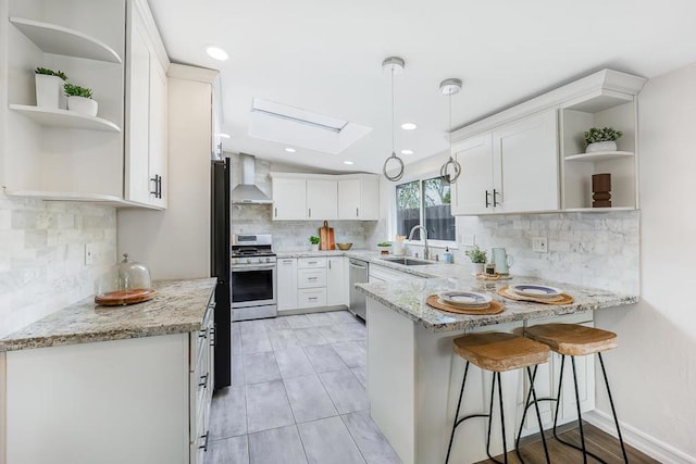 kitchen with light stone counters, white cabinetry, kitchen peninsula, and wall chimney range hood