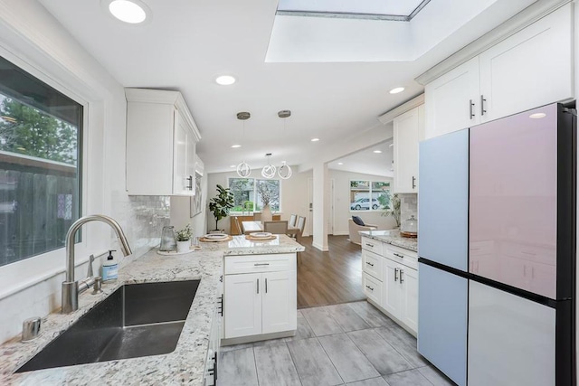 kitchen with light stone countertops, white cabinetry, fridge, and sink