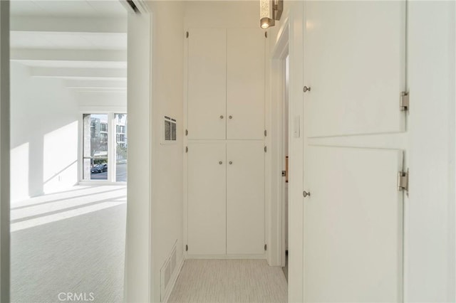 corridor featuring beamed ceiling and light colored carpet