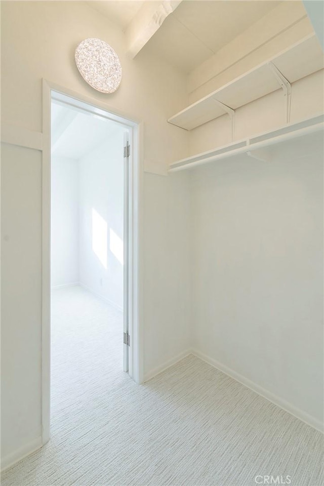 walk in closet featuring light carpet and beamed ceiling