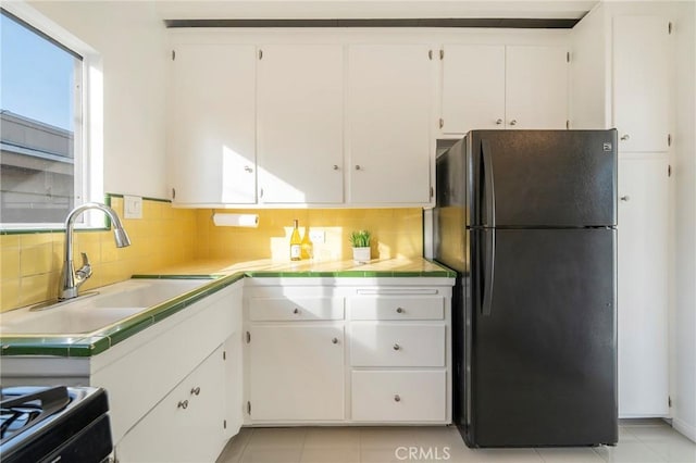 kitchen featuring white cabinetry, sink, tasteful backsplash, and black fridge