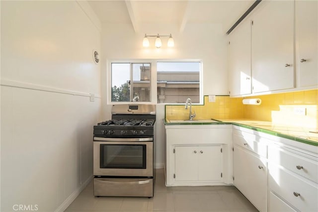 kitchen featuring sink, stainless steel gas range, white cabinetry, beam ceiling, and tasteful backsplash