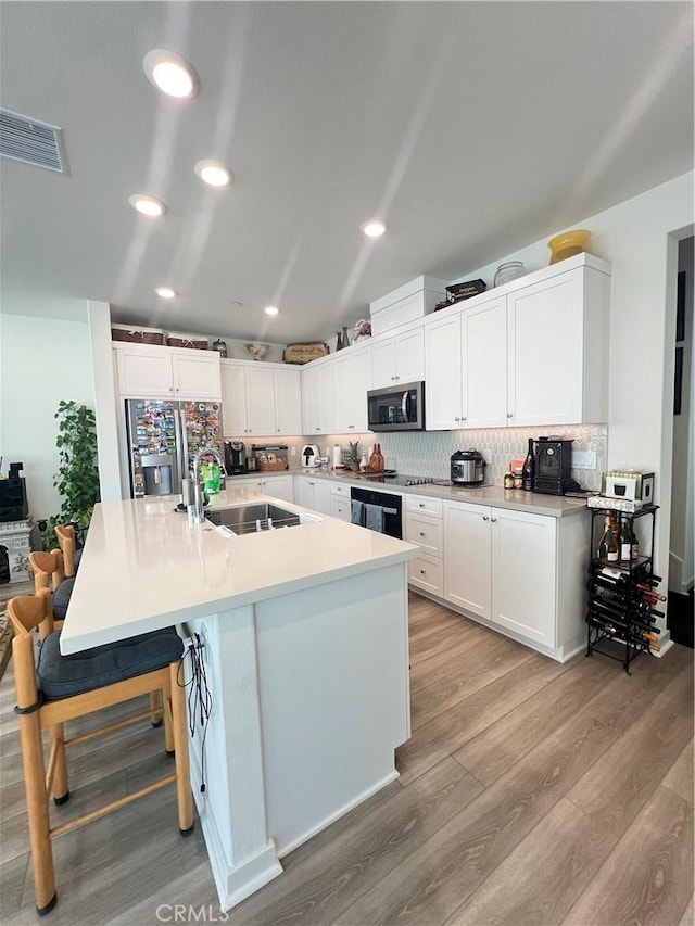 kitchen with sink, a breakfast bar area, stainless steel appliances, an island with sink, and white cabinets