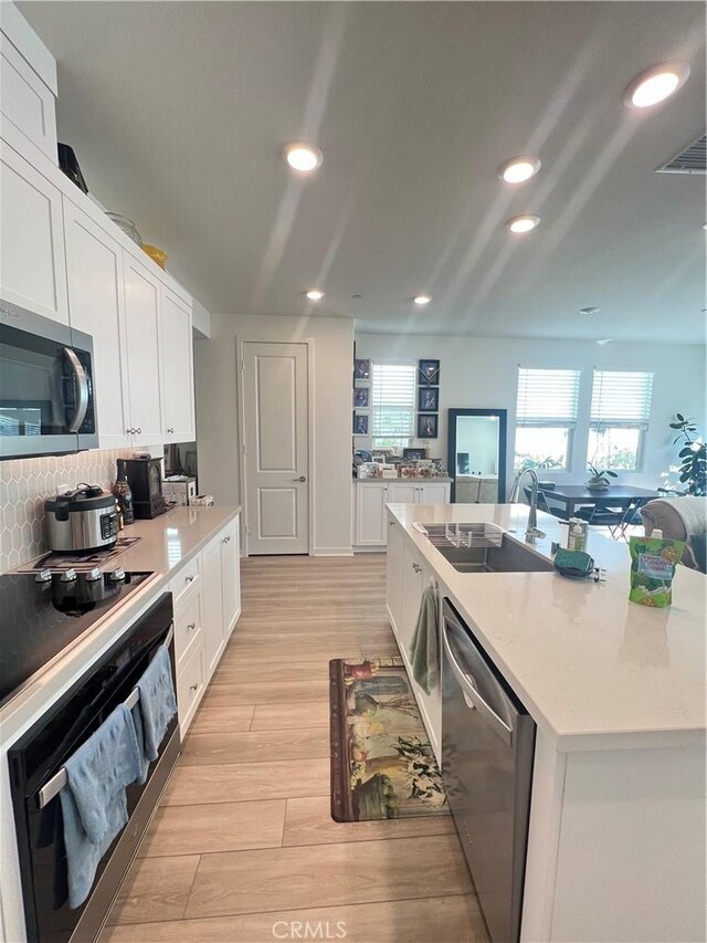 kitchen with sink, white cabinetry, appliances with stainless steel finishes, light hardwood / wood-style floors, and decorative backsplash