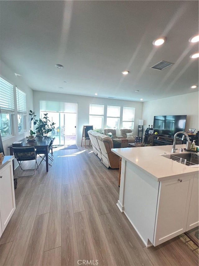 kitchen featuring sink, a center island with sink, white cabinets, and light hardwood / wood-style flooring