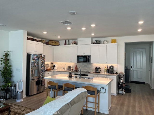 kitchen with appliances with stainless steel finishes, a kitchen island with sink, backsplash, white cabinetry, and light wood-type flooring