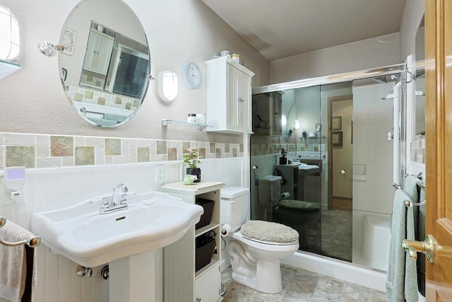 bathroom with a stall shower, a wainscoted wall, a sink, and toilet